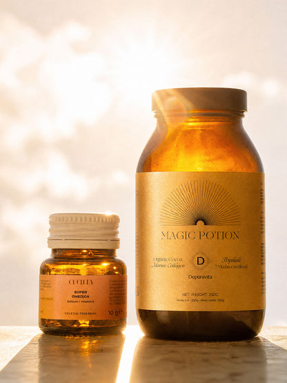 Two amber glass supplement bottles on a reflective surface with a warm, sunlit bokeh background. The larger bottle on the right is labeled &