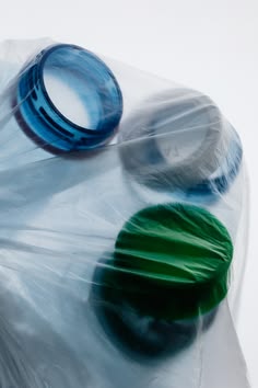 Three plastic bottle caps in blue, gray, and green, wrapped together in a translucent clear plastic bag against a white background.