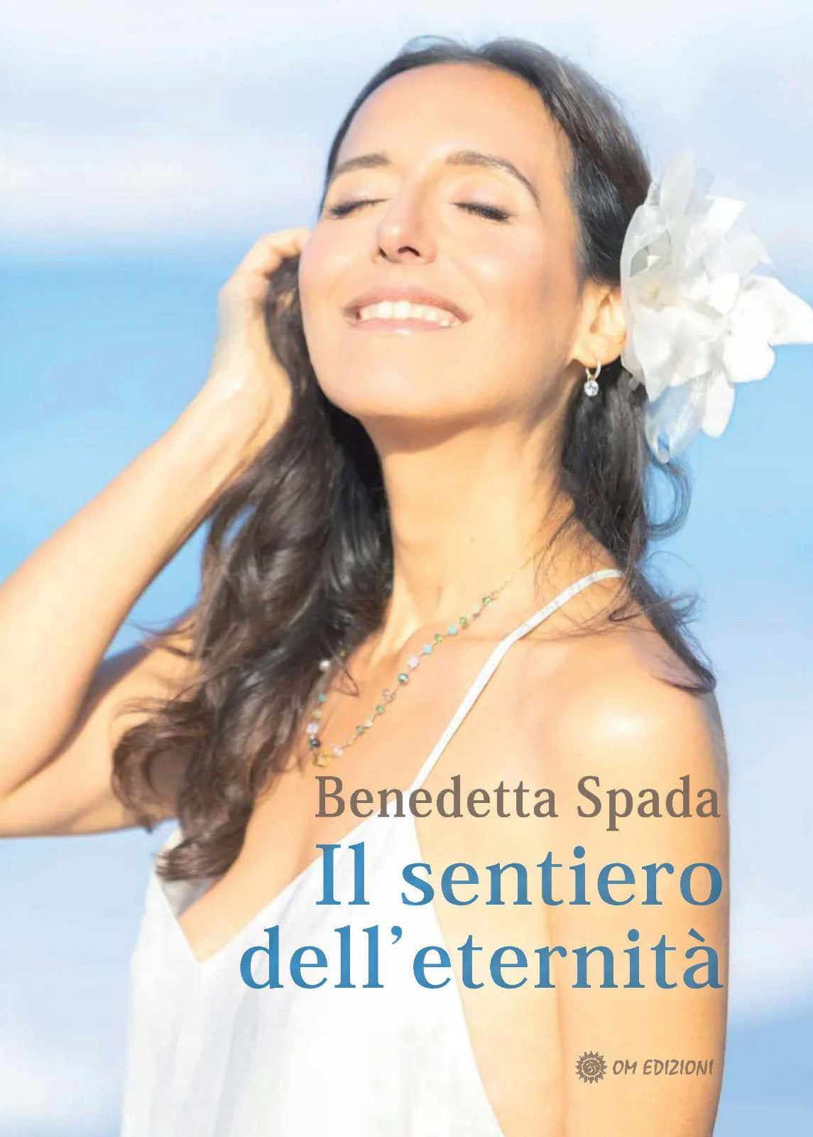 Book cover for 'Il sentiero dell'eternità' by Benedetta Spada, featuring a smiling woman with closed eyes against a bright blue sky, with a white flower in her hair and the title text overlaid.