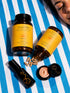 Two bottles of Moon Skin skincare products and a small black tube are arranged on a blue-and-white striped blanket, with one bottle tipped over to spill capsules. A woman&